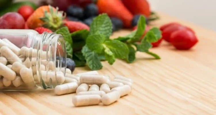 Vitamini, biljni i drugi djelatni sastojci u strategiji suplementacije Staklena bočica iz koje ispadaju kapsule s vitaminima i mineralima. U pozadini se nalazi voće i povrće